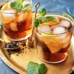cold brewed black tea in glasses on a table garnished with mint and orange