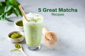 Matcha latte surronded by a matcha whisk and matcha on a spoon on a grey table