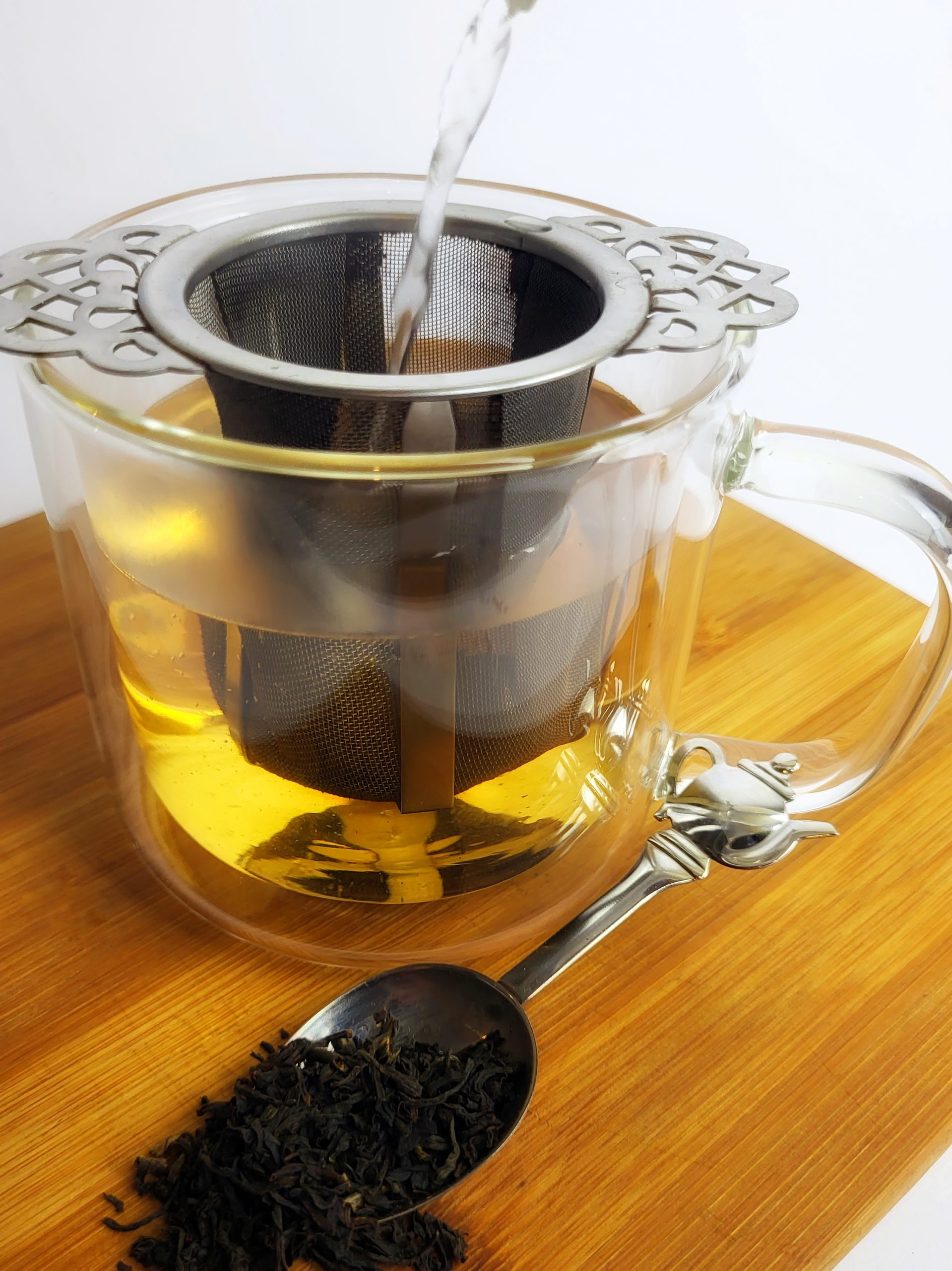 water being poured onto loose leaf tea leaves in a glass cup