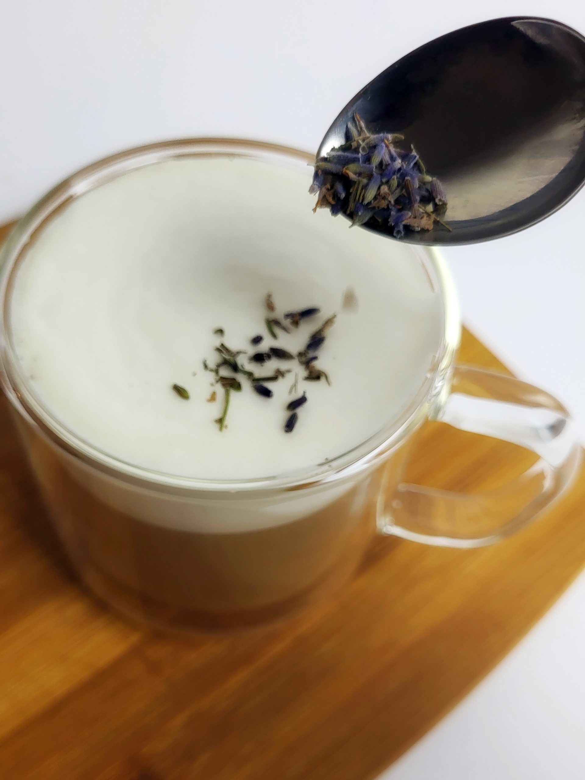 a teaspoon sprinkling dried lavender flowers on top of a tea latte
