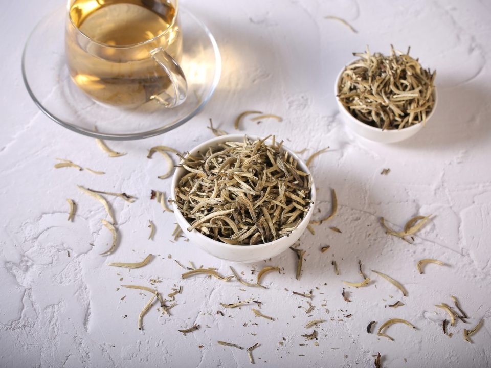 white tea leaves in a glass cup and pot on a white background