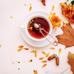 autumn leaves surrounding a cup of loose leaf tea on a white table